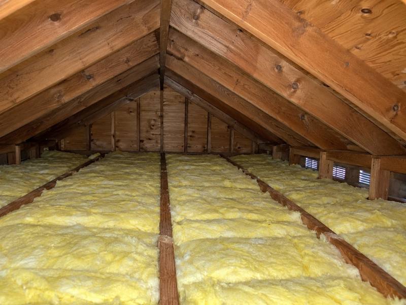 Yellow batts running the length of an attic toward a gable end with louvred vents
