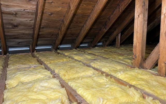 Yellow batts along the low eave edge of an older attic with dark board sheathing overhead