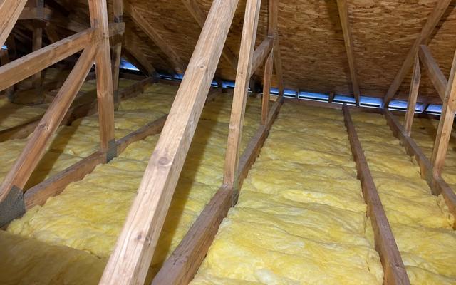 Yellow batts between attic joists with diagonal truss braces and soffit vents along the roofline