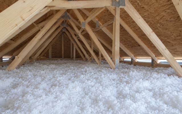 Fluffy white loose-fill insulation blown deep across an attic floor under new roof trusses