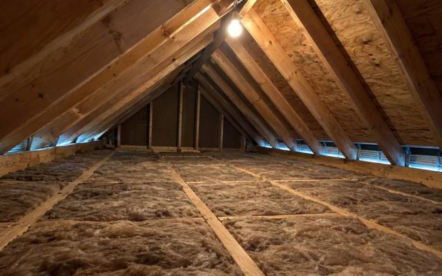 Brown batts between the joists of a newer attic with a row of vents along the eaves