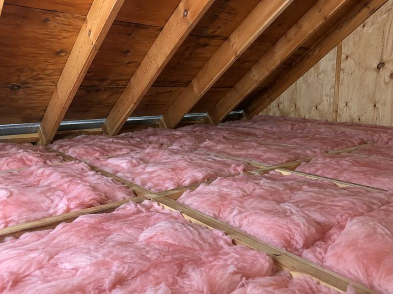 Pink fibreglass batts fitted across an attic floor beside a plywood gable wall